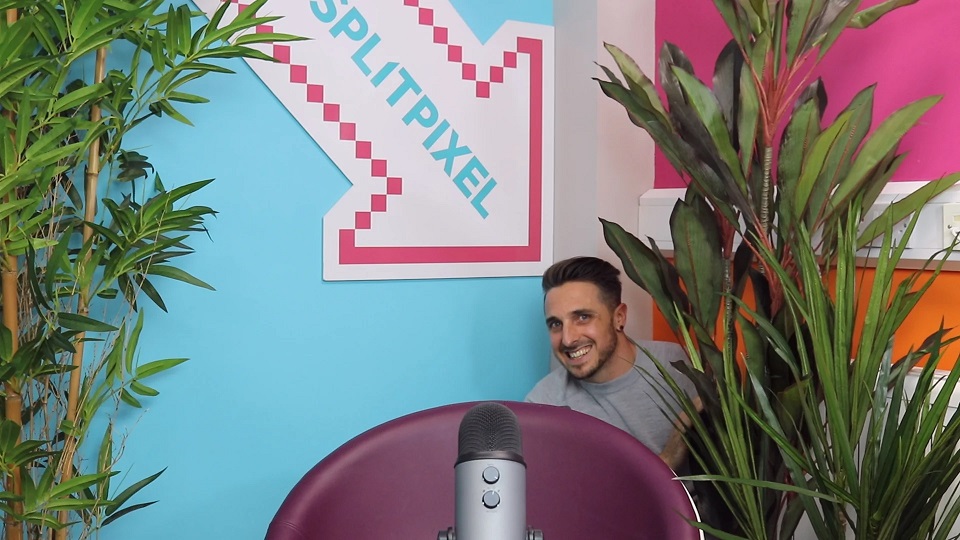 Image of a man hiding behind a chair, with a giant branded arrow pointing at him. In the forground there is a chair and a microphone. 