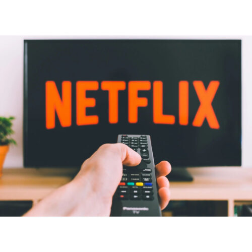 A hand holding a remote pointing it at a TV screen with the Netflix logo on it