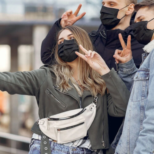 A group pf people posing for a selfie, putting the peace sign and wearing face masks