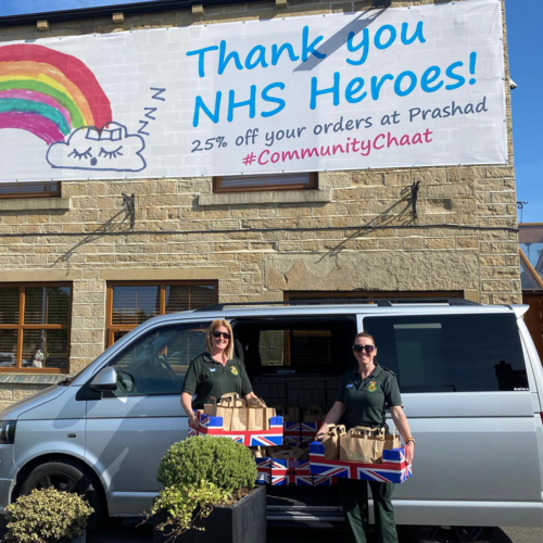 A large NHS Heroes banner and two NHS workers with boxes of brown bags smiling