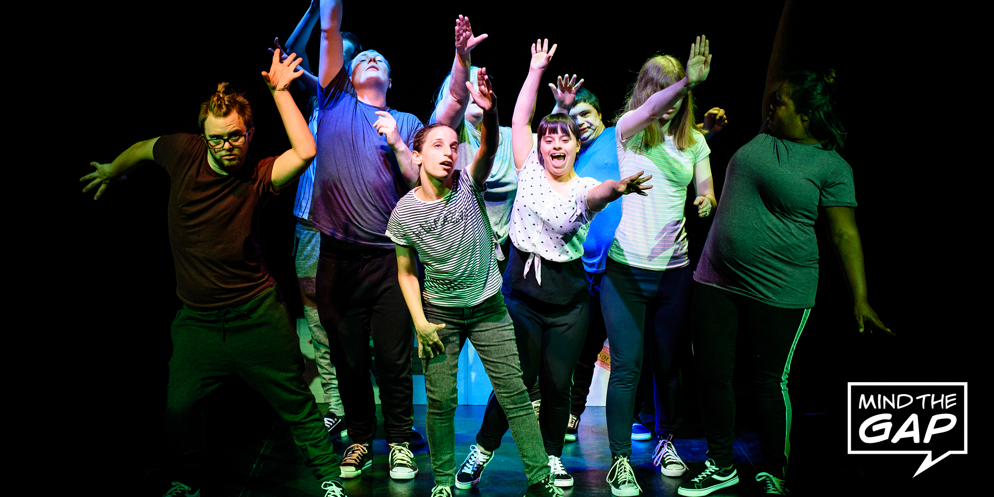 Theatre performers on stage reaching into the audience, with the Mind The Gap logo in the bottom right
