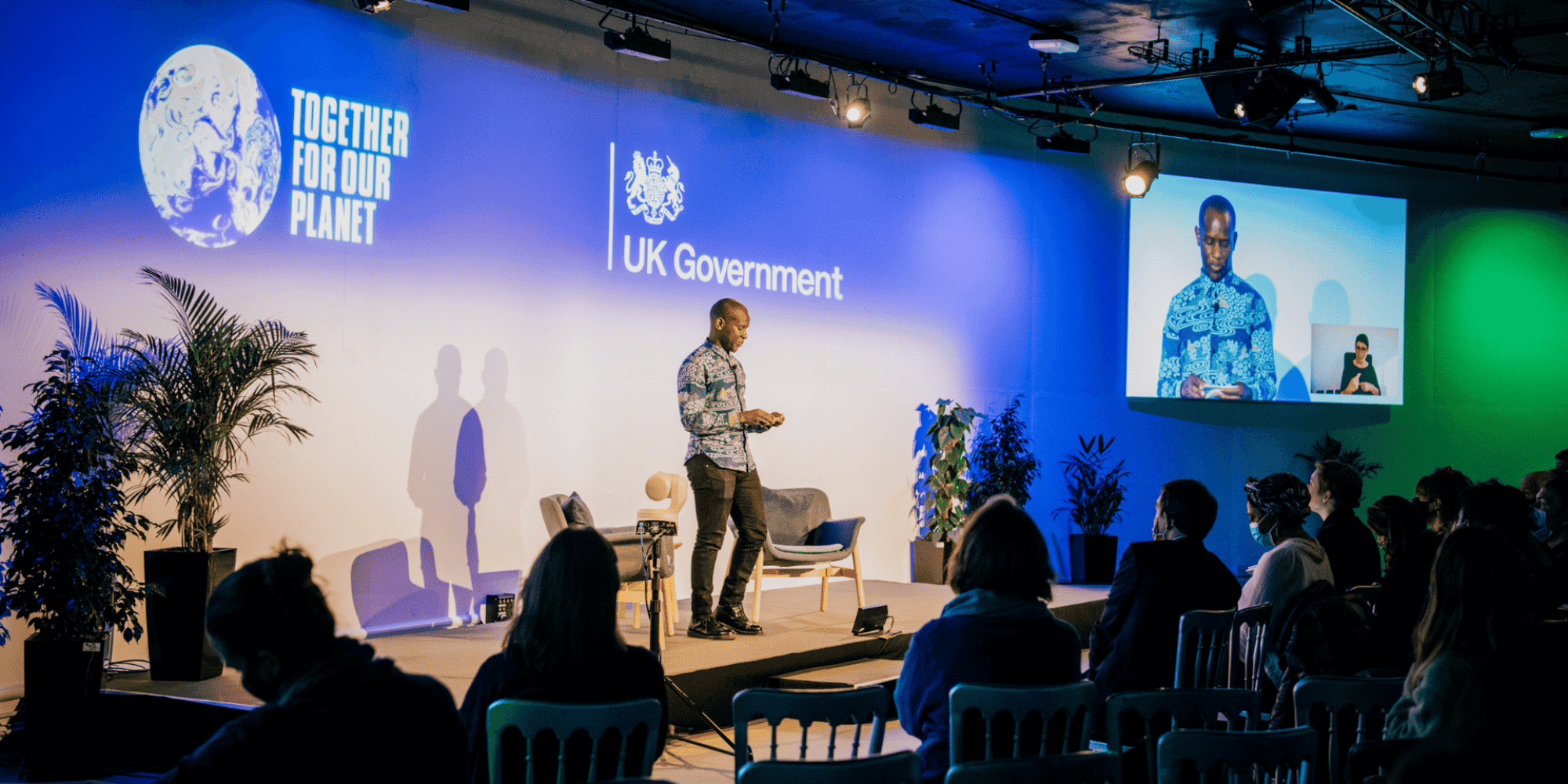 A person on stage talking with the UK Government logo behind