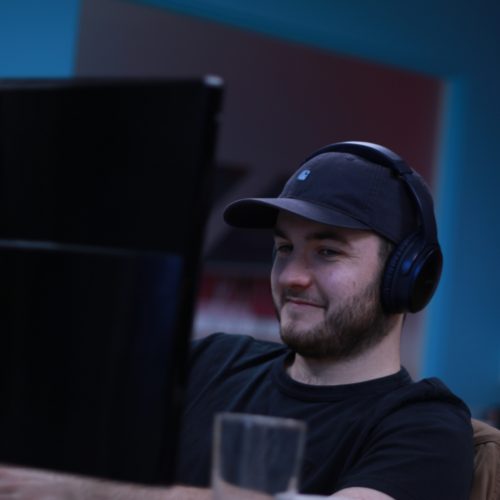 A man wearing headphones and a cap looking at a computer screen