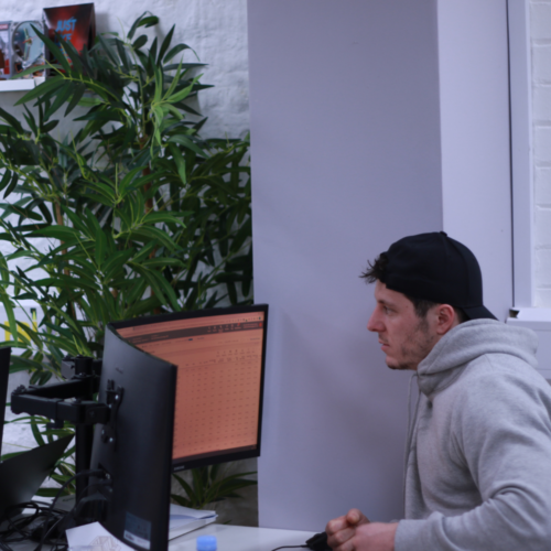 A man wearing a cap backwards looking at two computer screens
