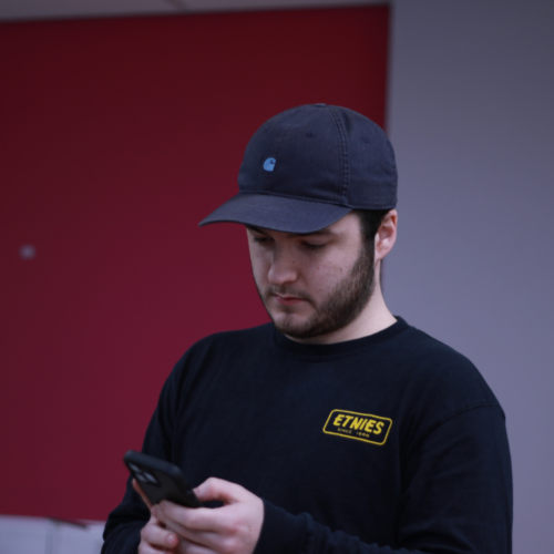 Image of a man holding a phone, wearing a cap and Etnies t-shirt