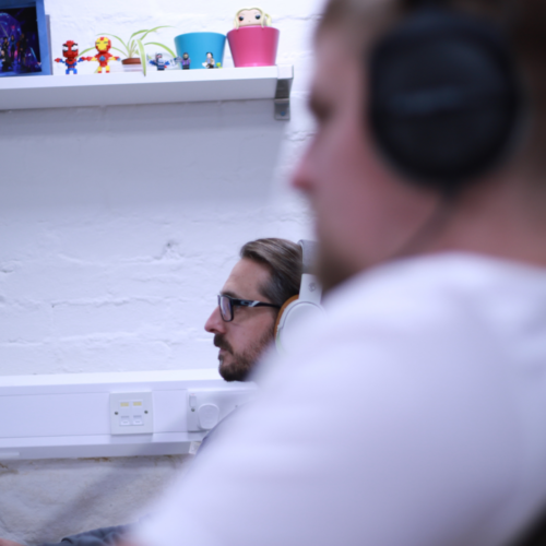 Two men looking at computer screens wearing headphones