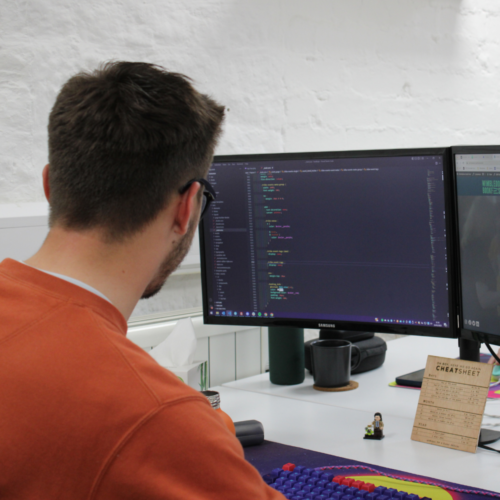 A man looking at a computer screen showing coding, from behind