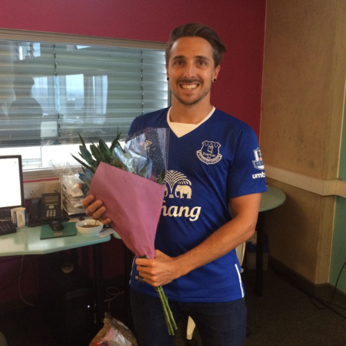 Job smiling holding a bouquet of flowers and wearing an Everton shirt