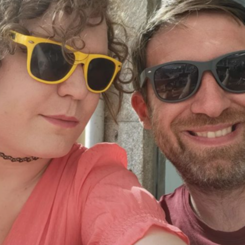 A selfie of Ren and Greg, the project manager and technical director at Splitpixel respectively. Ren is a trans woman in yellow sunglasses, Greg is a beardy man in black sunglasses. Greg is smiling, Ren looks annoyed